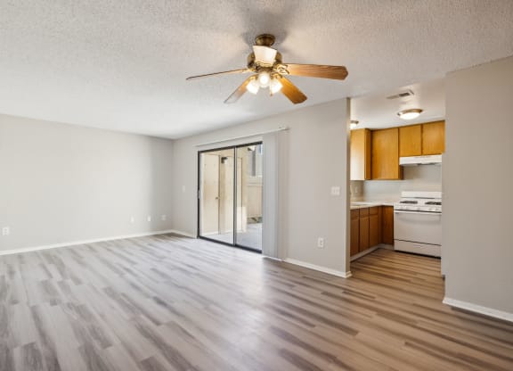 an empty living room with a ceiling fan and a kitchen