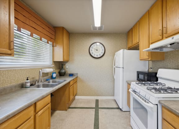 a kitchen with white appliances and wooden cabinets and a clock on the wall