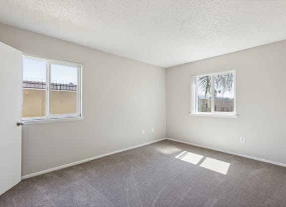 an empty living room with two windows and carpeting