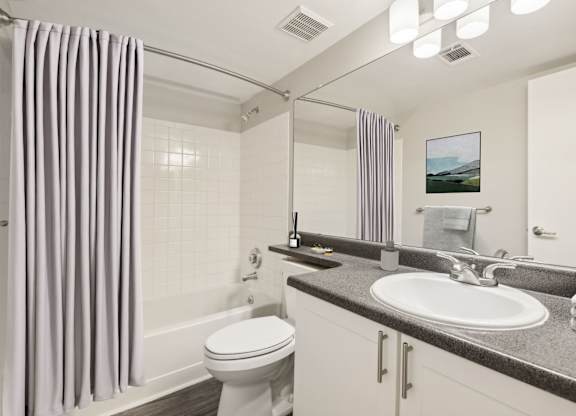A bathroom with a white toilet, a sink, and a shower with a grey curtain.