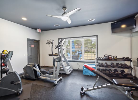 a gym with weights and a ceiling fan and a window