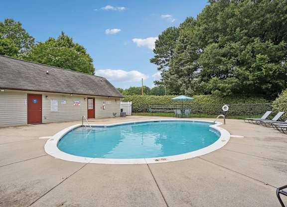 A small pool with a blue umbrella and a building with a red door in the background.