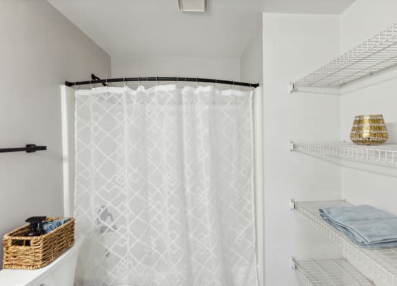 a shower with a white shower curtain and shelves with towels