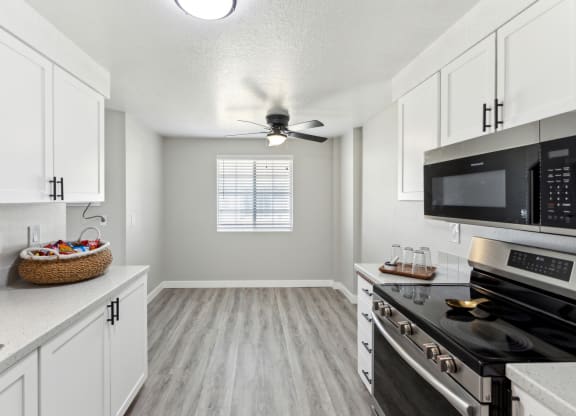 an empty kitchen with white cabinets and black appliances and a ceiling fan