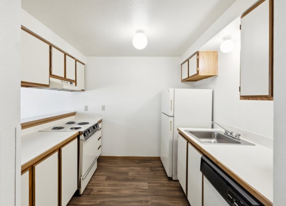 an empty kitchen with white appliances and wood flooring
