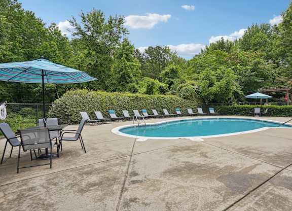 A pool surrounded by trees and chairs.