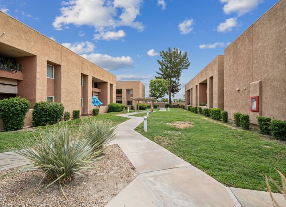 a walkway between two buildings with grass and a sidewalk