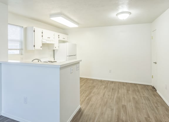 an empty kitchen and living room with white cabinets and wood flooring