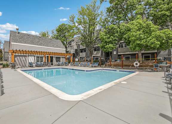 A large outdoor swimming pool surrounded by a concrete patio and lounge chairs.