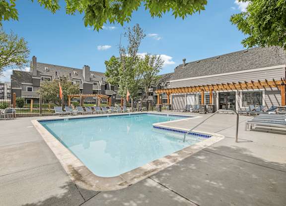 A large swimming pool surrounded by a concrete patio and a wooden pergola.