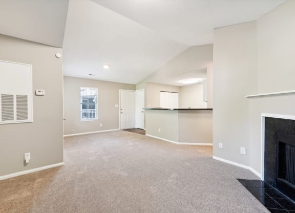 an empty living room with a fireplace and a kitchen