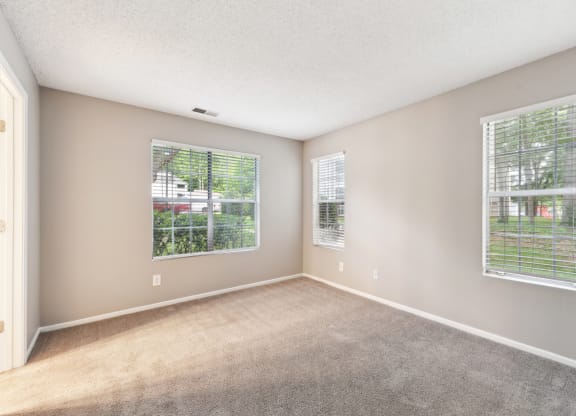 an empty living room with two windows and carpeting