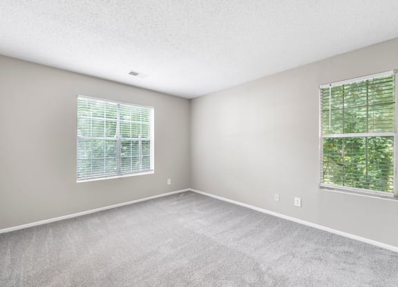 an empty bedroom with two windows and carpeting