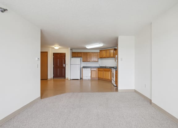 an empty living room and kitchen with white appliances and wood cabinets