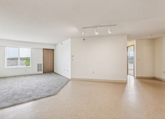 the living room and dining room of an apartment with white walls and beige carpet