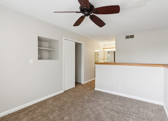 an empty living room with a ceiling fan and a white wall