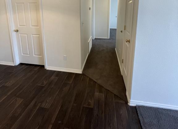 A hallway with white walls and dark wood flooring.