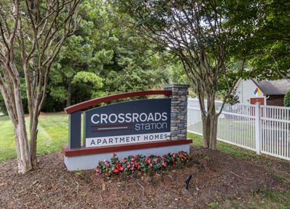 a sign for the crossroads station in front of a fence and trees