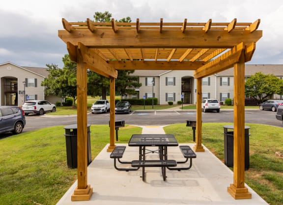 a picnic table under a wooden pavilion on a sidewalk