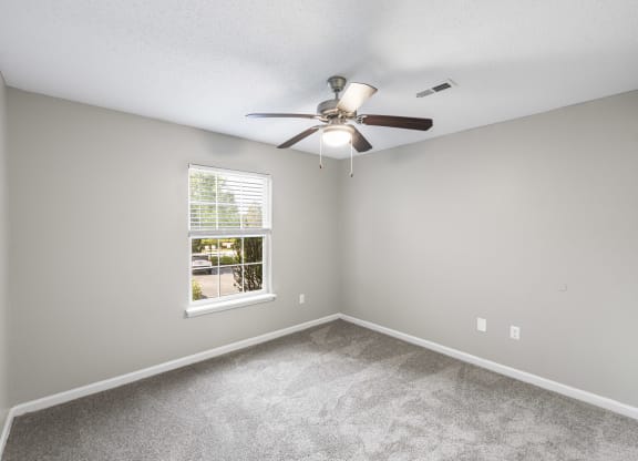 an empty bedroom with a ceiling fan and a window