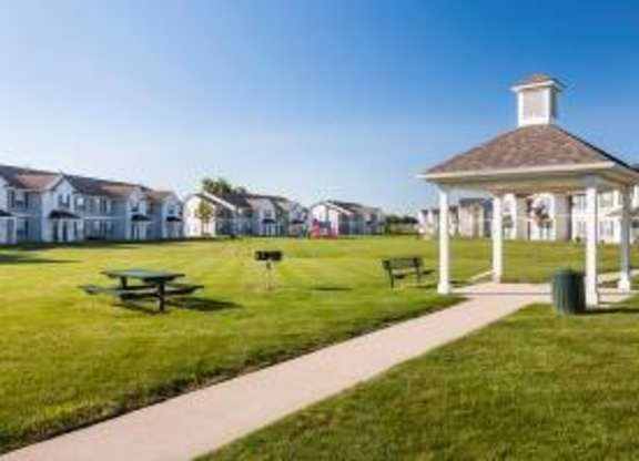 A gazebo is situated in the middle of a grassy area with a picnic table and bench.