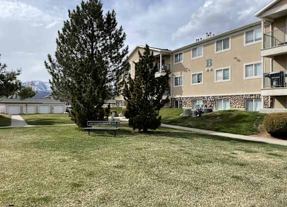 A grassy area with a bench and trees in front of apartment buildings.