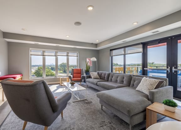 A modern living room with a grey sofa, a red chair, and a large window.