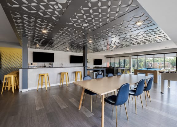 a communal area with a long table and chairs and a bar and television