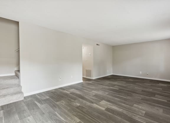 A room with a wooden floor and a staircase on the left side.