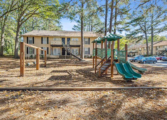 A playground with a green slide and a wooden swing set.