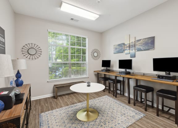 a living room with desks and chairs and a table with computer monitors
