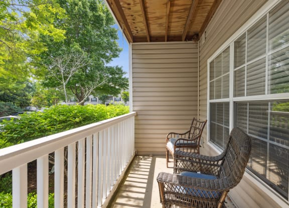 two wicker chairs on a porch with a view of the yard and trees
