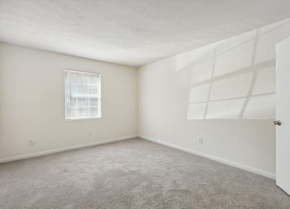 an empty bedroom with white walls and carpet and a window