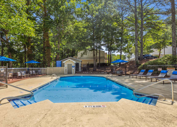 our resort style swimming pool is surrounded by chairs and trees