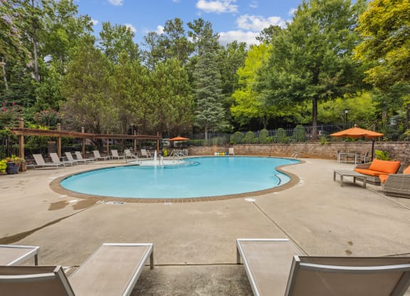 a swimming pool with chairs and trees in the background