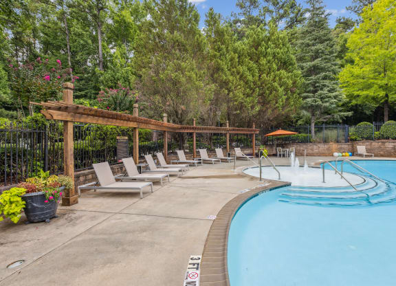 a swimming pool with chairs around it and trees in the background