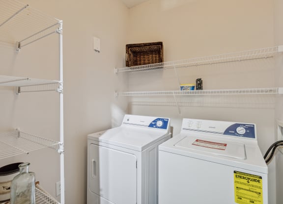the laundry room has two washes and a dryer in it and shelves above