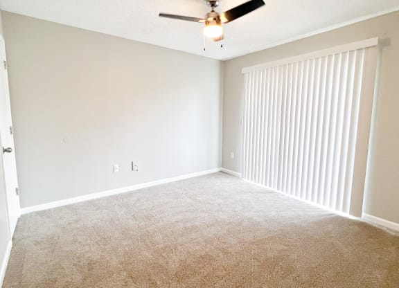 an empty bedroom with a ceiling fan and blinds