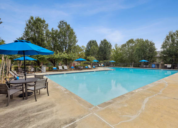 our resort style swimming pool is surrounded by patio furniture and umbrellas