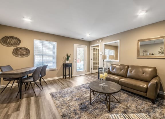 Modern lounge with a brown leather sofa, round coffee table, and dining area. Beige walls, wood flooring, and decorative accents create a cozy ambiance