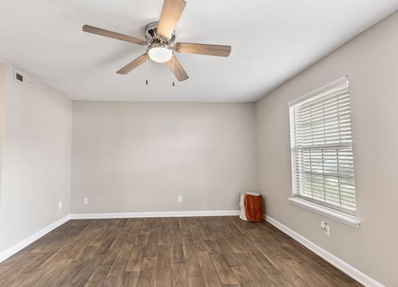 an empty living room with a ceiling fan and a window