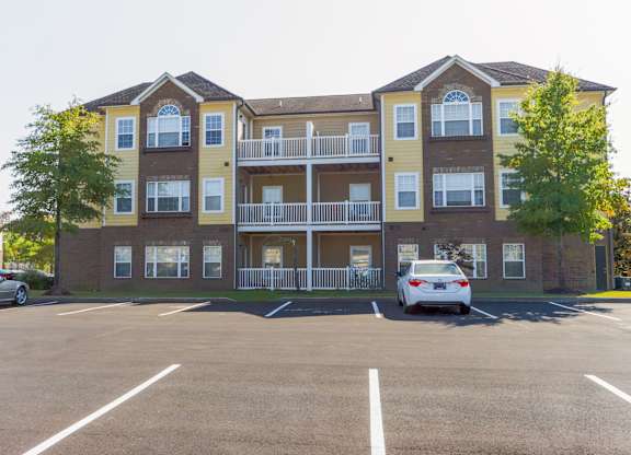 A parking lot in front of a two-story apartment building with cars parked.