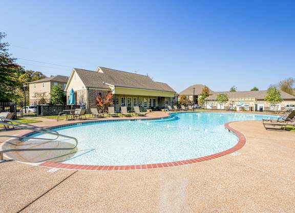 A large outdoor swimming pool with a red border and a small building in the background.