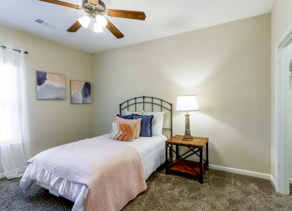 A bedroom with a bed, a table with a lamp, and two pictures on the wall.