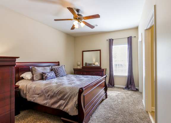 A bedroom with a bed, dresser, mirror, and window.