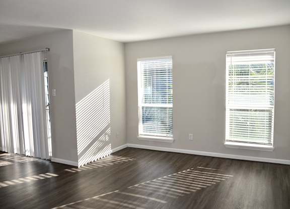 A room with wooden floors and two windows with blinds.