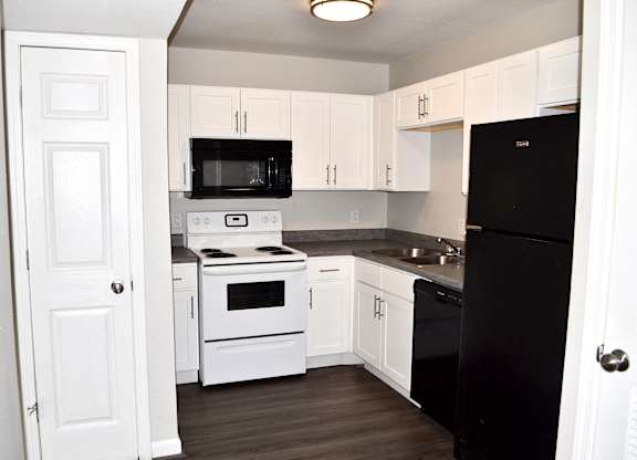 A black refrigerator is in a kitchen with white cabinets.