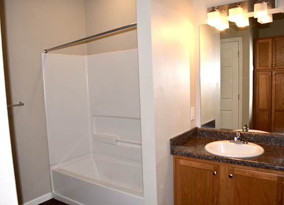 A white shower stall in a bathroom with a granite countertop and a mirror.
