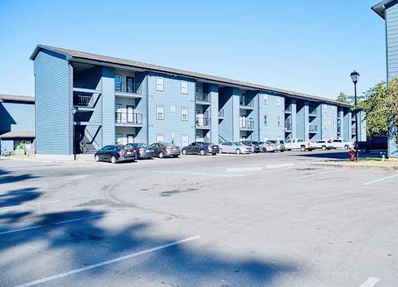 A parking lot in front of a blue building with cars parked.