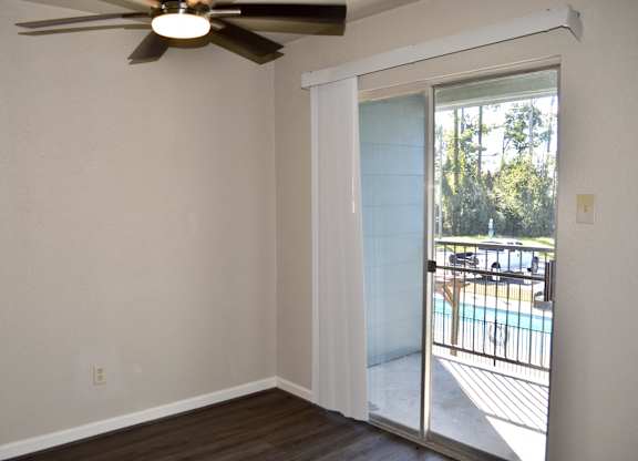 A room with a ceiling fan and sliding glass doors leading to a pool and trees.